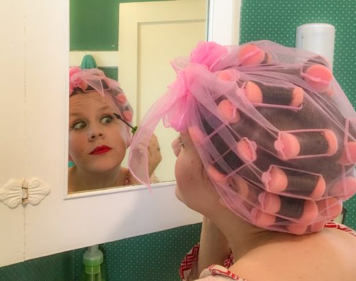 Woman with hair in rollers looking in mirror and applying makeup